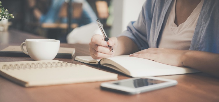 Woman writing in a notebook symbolising the development of healthy coping mechanisms in addiction recovery.