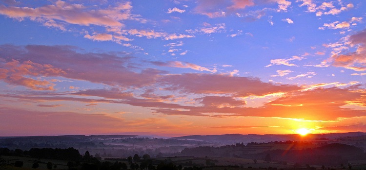 Sunrise over a mountain landscape with tall trees, symbolizing emotional resilience and healing in addiction recovery.